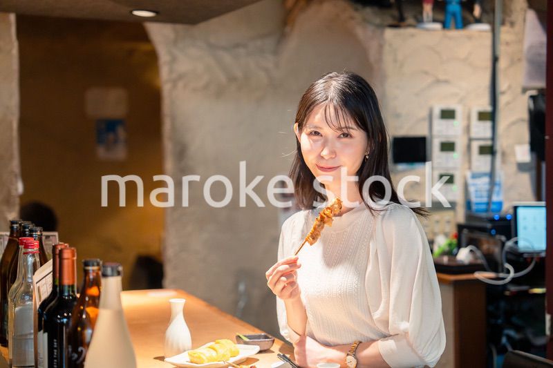 一人でカウンター席に座って焼き鳥を食べる女性