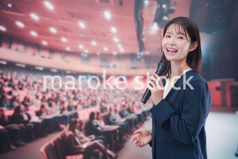大勢の聴衆が集まるホールで司会をする若い女性