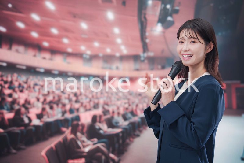 大勢の聴衆が集まるホールで司会をする若い女性