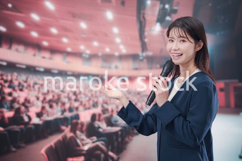 大勢の聴衆が集まるホールで司会をする若い女性