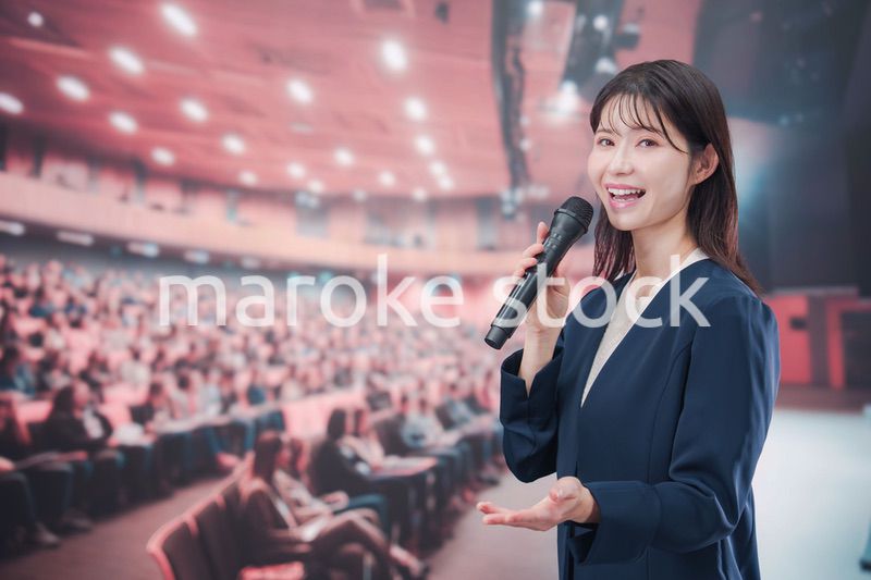 大勢の聴衆が集まるホールで司会をする若い女性