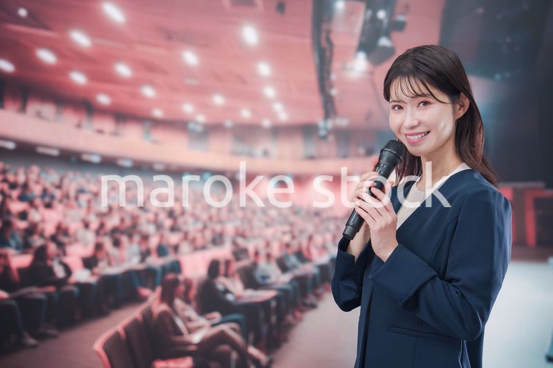 大勢の聴衆が集まるホールで司会をする若い女性