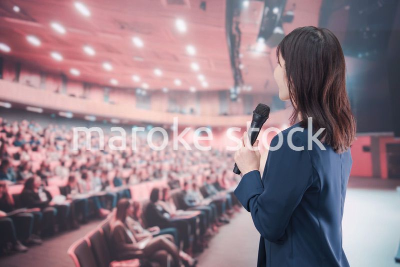 大勢の聴衆が集まるホールで司会をする若い女性