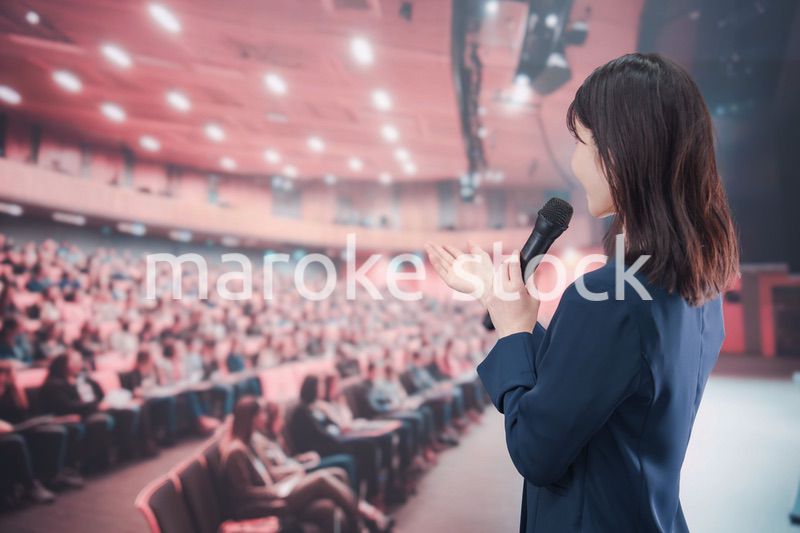 大勢の聴衆が集まるホールで司会をする若い女性