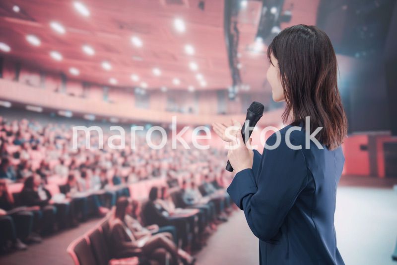 大勢の聴衆が集まるホールで司会をする若い女性