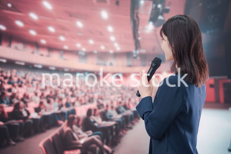 大勢の聴衆が集まるホールで司会をする若い女性