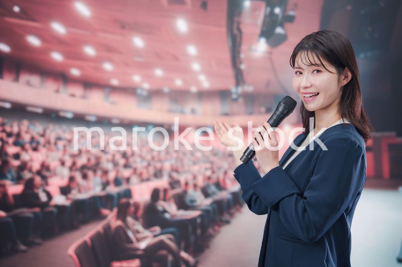 大勢の聴衆が集まるホールで司会をする若い女性