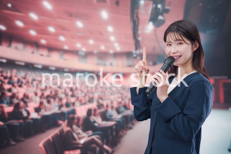 大勢の聴衆が集まるホールで司会をする若い女性