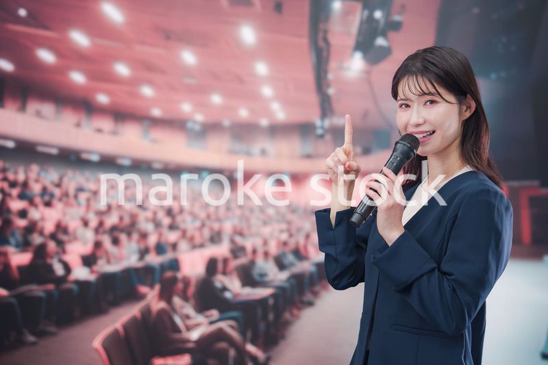 大勢の聴衆が集まるホールで司会をする若い女性
