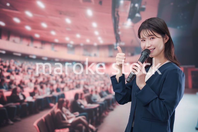 大勢の聴衆が集まるホールで司会をする若い女性