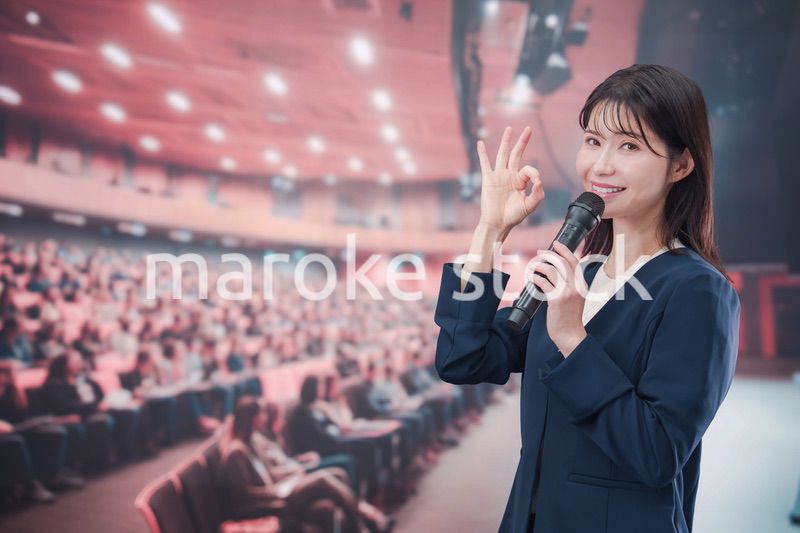 大勢の聴衆が集まるホールで司会をする若い女性