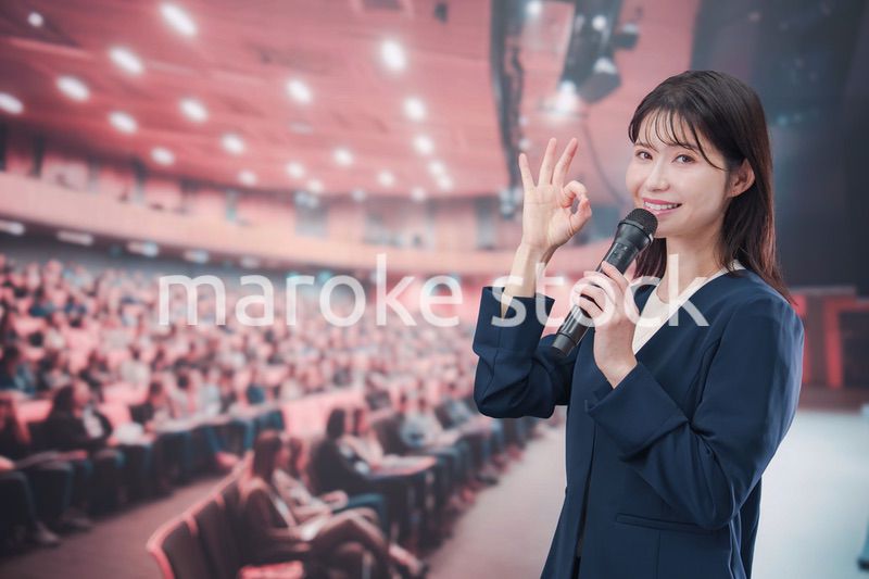 大勢の聴衆が集まるホールで司会をする若い女性