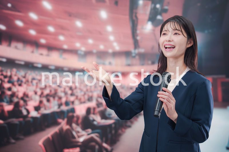 大勢の聴衆が集まるホールで司会をする若い女性