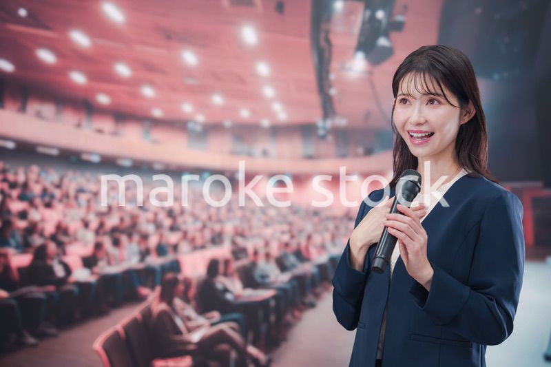 大勢の聴衆が集まるホールで司会をする若い女性