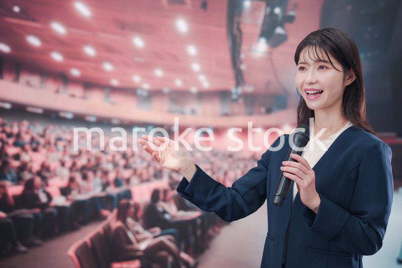 大勢の聴衆が集まるホールで司会をする若い女性