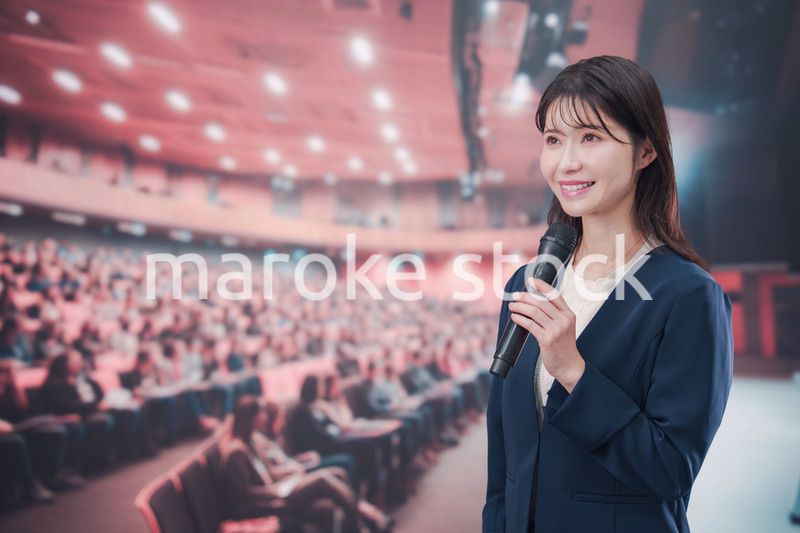 大勢の聴衆が集まるホールで司会をする若い女性