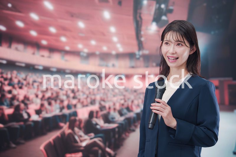 大勢の聴衆が集まるホールで司会をする若い女性