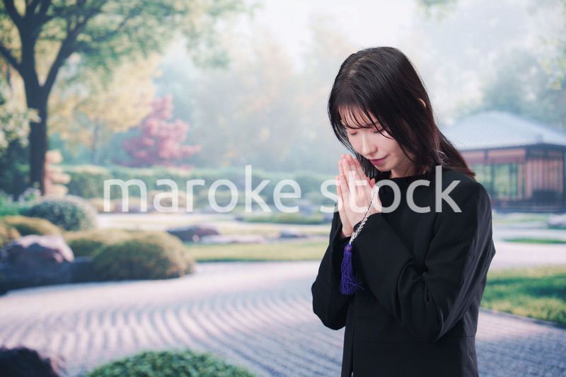 喪服を着て数珠を持って手を合わせる女性