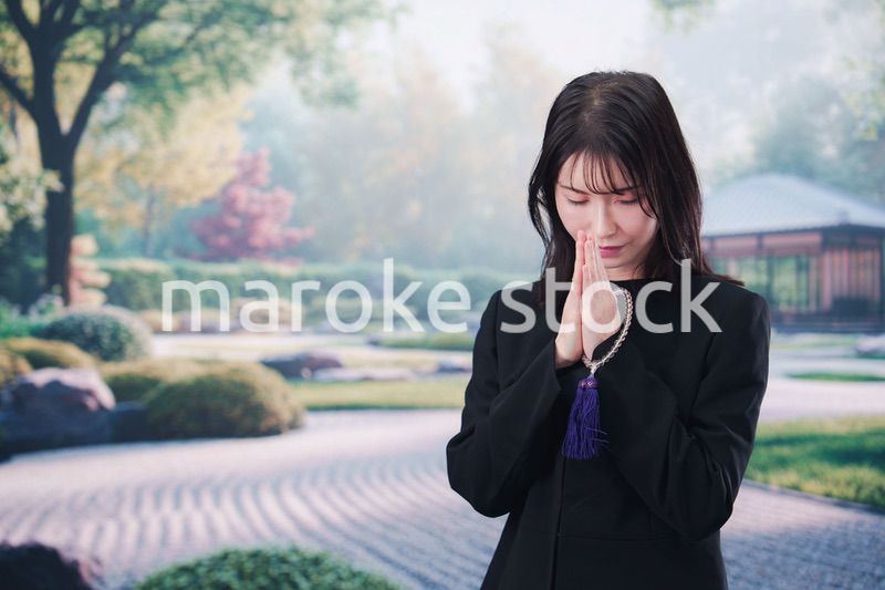 喪服を着て数珠を持って手を合わせる女性
