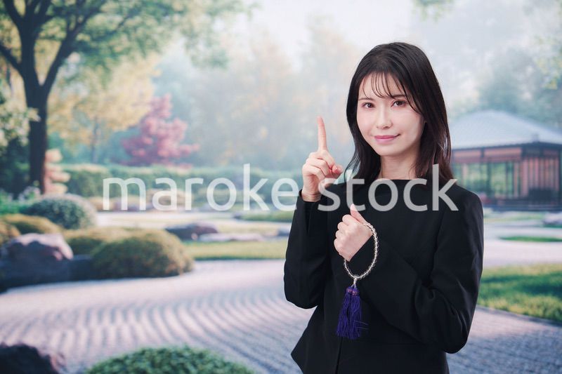 喪服を着て数珠を持って手を合わせる女性