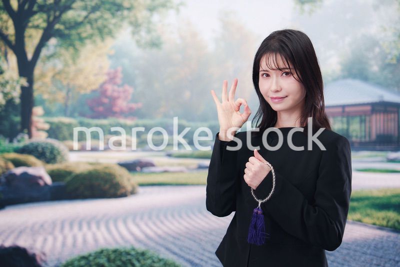 喪服を着て数珠を持って手を合わせる女性