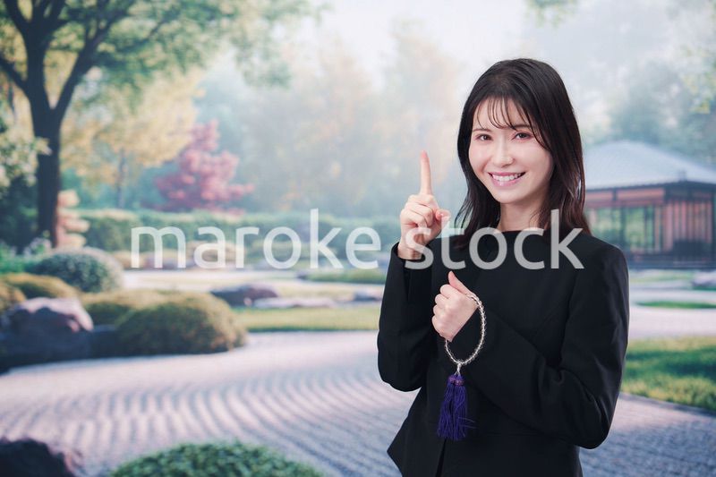 喪服を着て数珠を持って手を合わせる女性