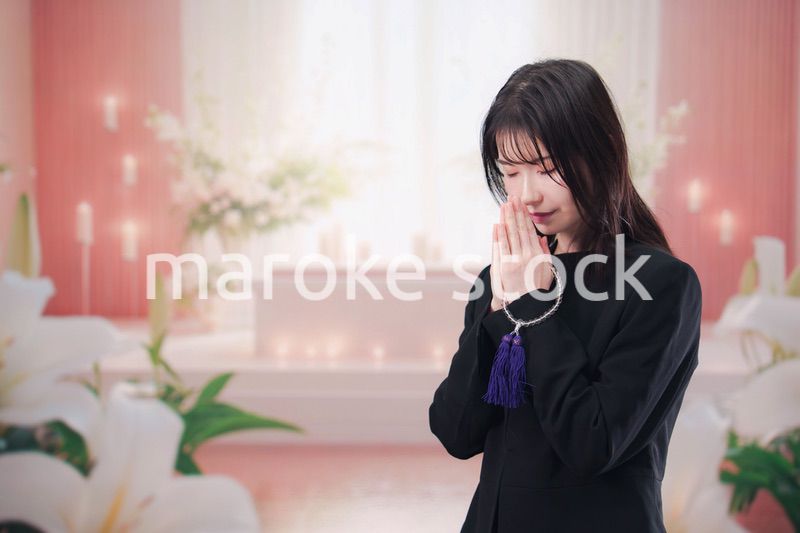 お葬式・お通夜で喪服を着て合掌をする若い女性