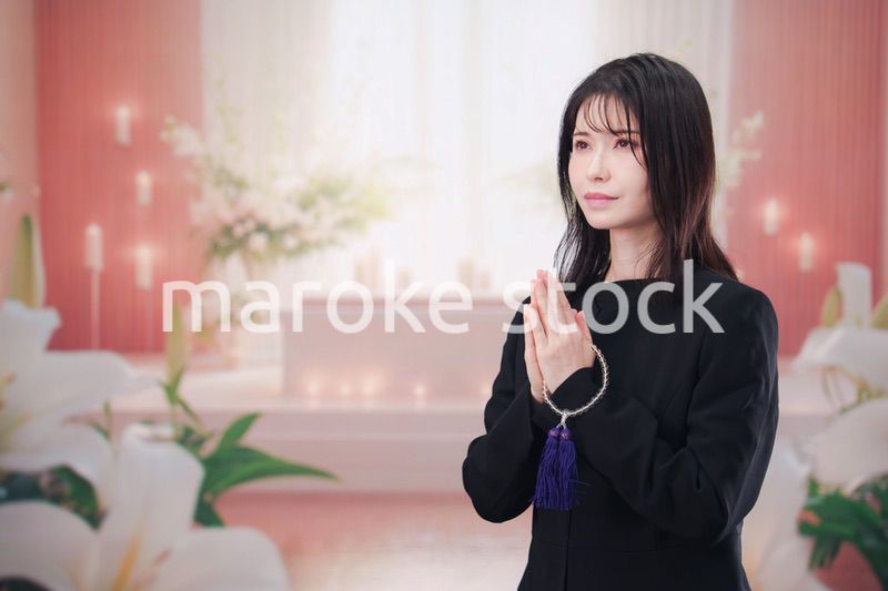 お葬式・お通夜で喪服を着て合掌をする若い女性