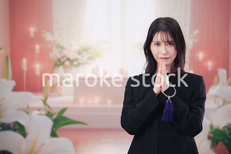 お葬式・お通夜で喪服を着て合掌をする若い女性