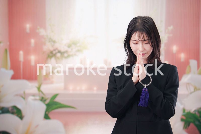 お葬式・お通夜で喪服を着て合掌をする若い女性