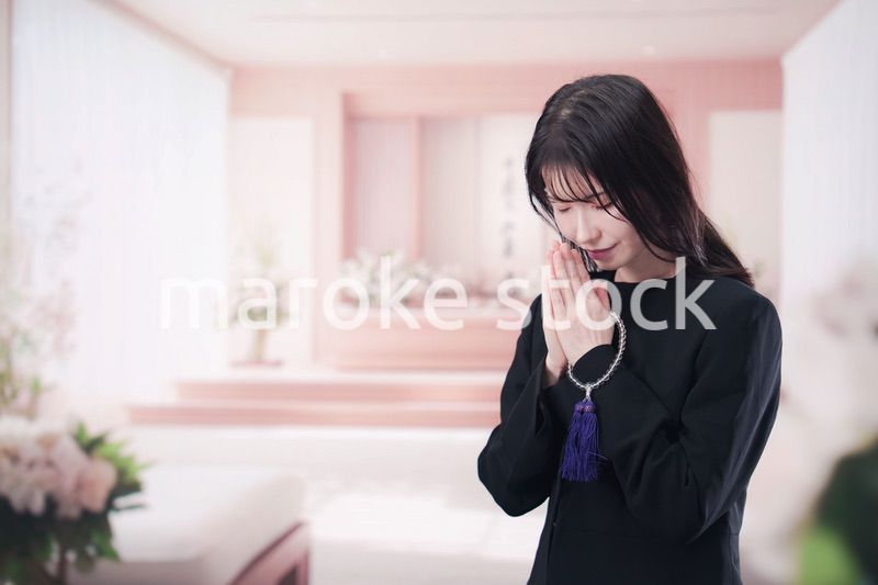 お葬式で合掌をする喪服を着た若い女性