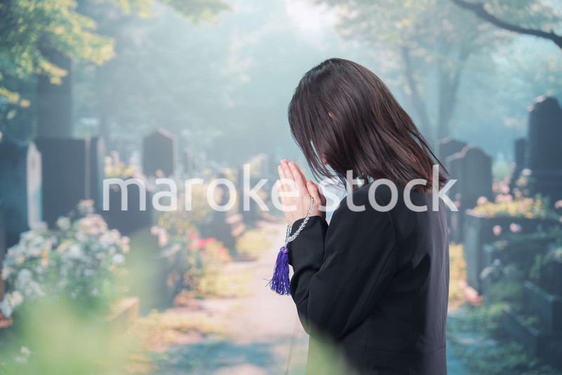 喪服を着て墓地で手を合わせる女性