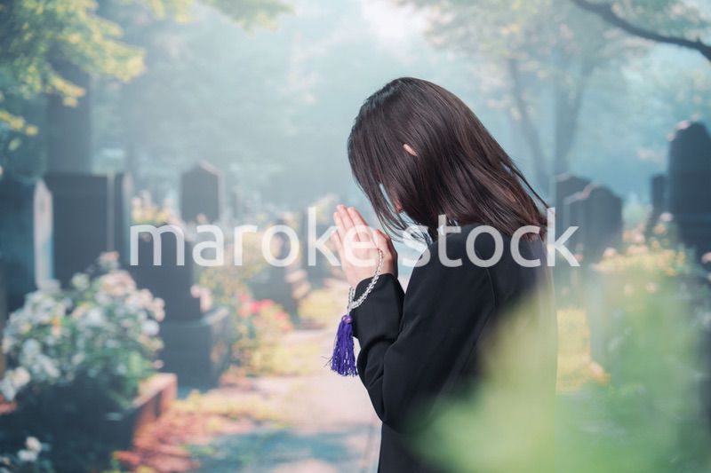 喪服を着て墓地で手を合わせる女性