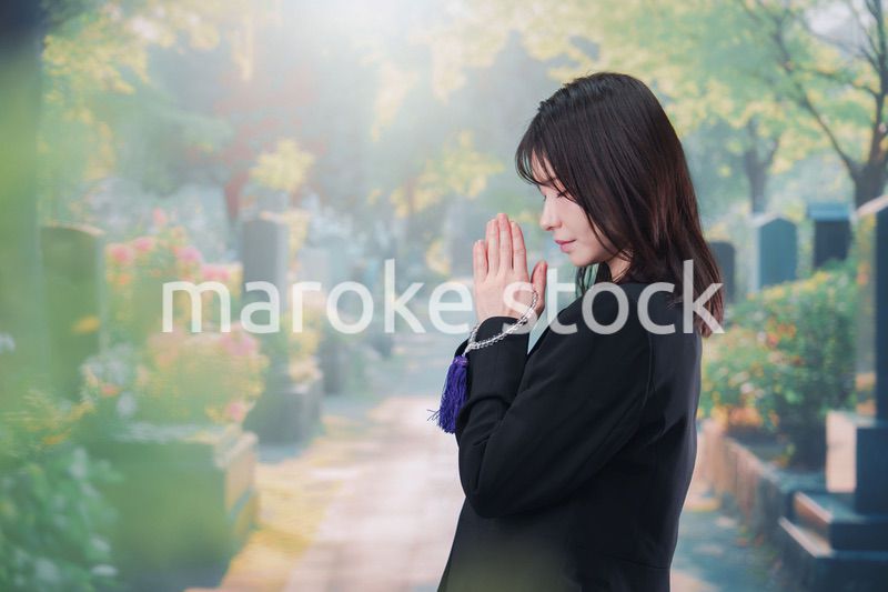 喪服を着て墓地で手を合わせる女性