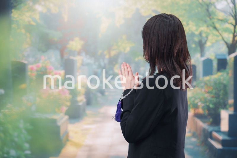 喪服を着て墓地で手を合わせる女性