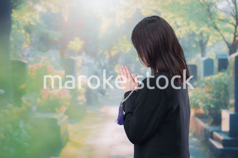 喪服を着て墓地で手を合わせる女性