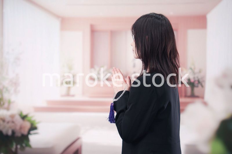 お葬式で合掌をする喪服を着た若い女性