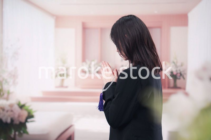 お葬式で合掌をする喪服を着た若い女性