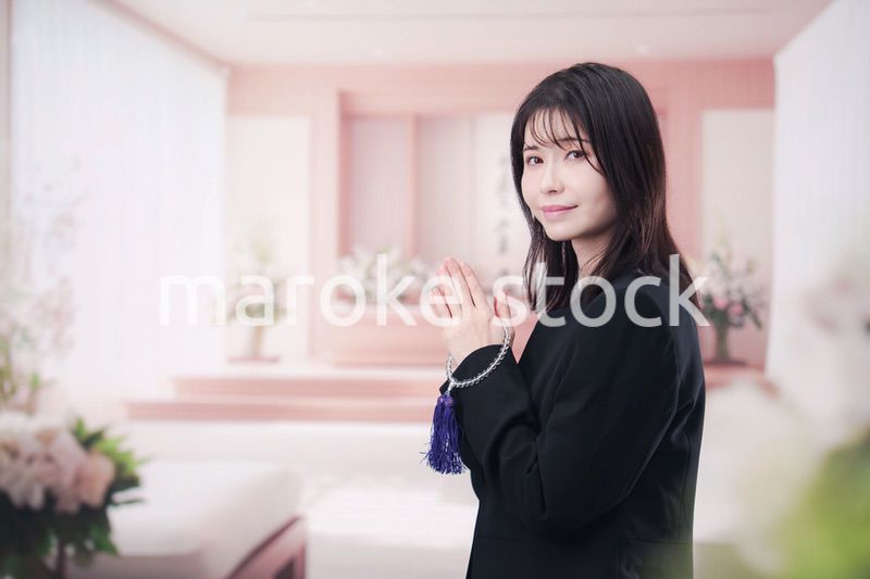 お葬式で合掌をする喪服を着た若い女性