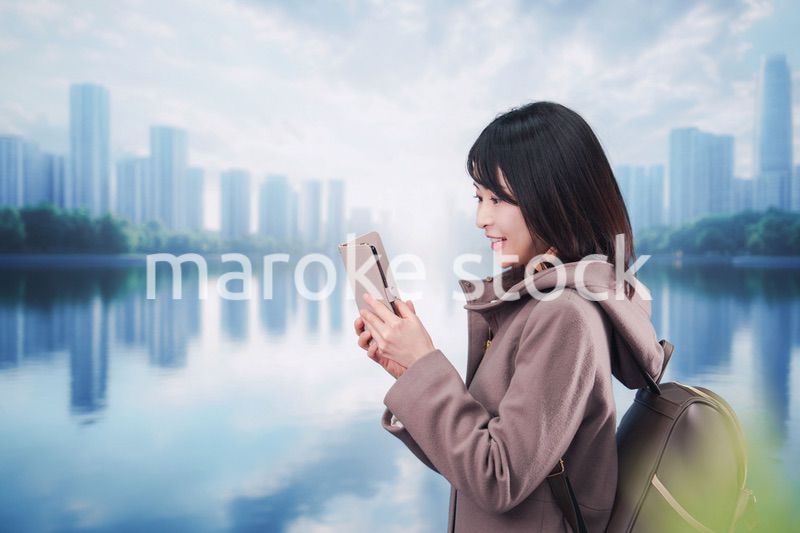 コートを着てスマホを使いながら外を歩く若い女性