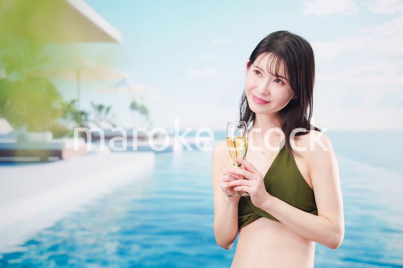 リゾートのプールで水着を着てスパークリングワインを飲む若い女性