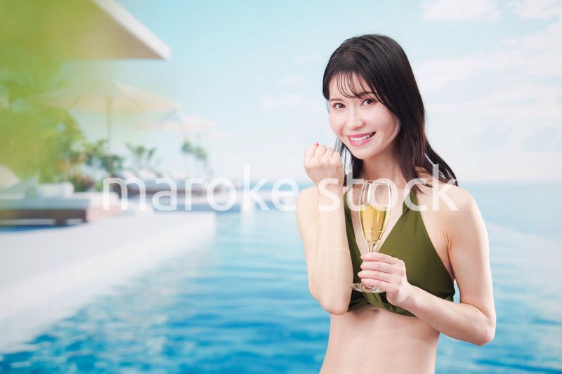 リゾートのプールで水着を着てスパークリングワインを飲む若い女性