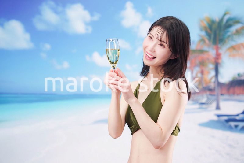 真夏のビーチでスパークリングワインを飲む水着を着た若い女性