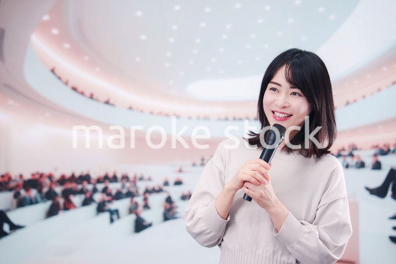 大勢の聴衆の前でマイクで話す女性