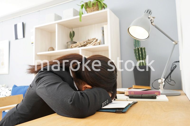 スーツを着て机で寝る女性