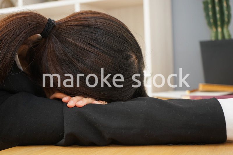 スーツを着て机で寝る女性