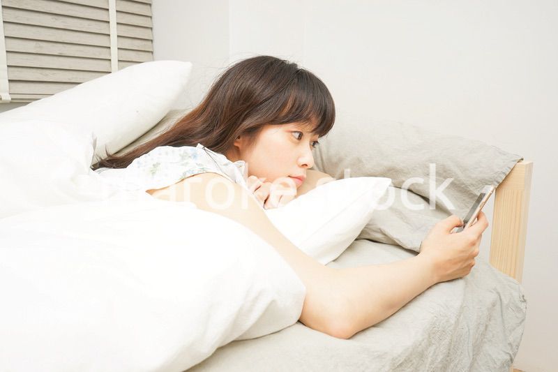 寝る前に携帯を使う若い女性