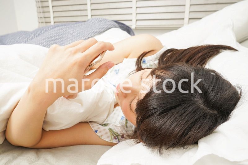 寝る前に携帯を使う若い女性