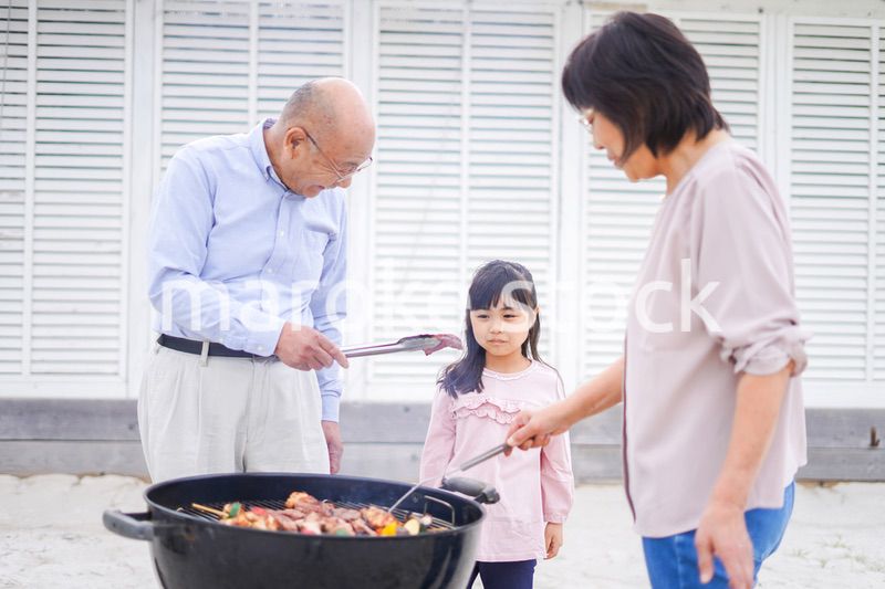 孫とバーベキューをする高齢の夫婦