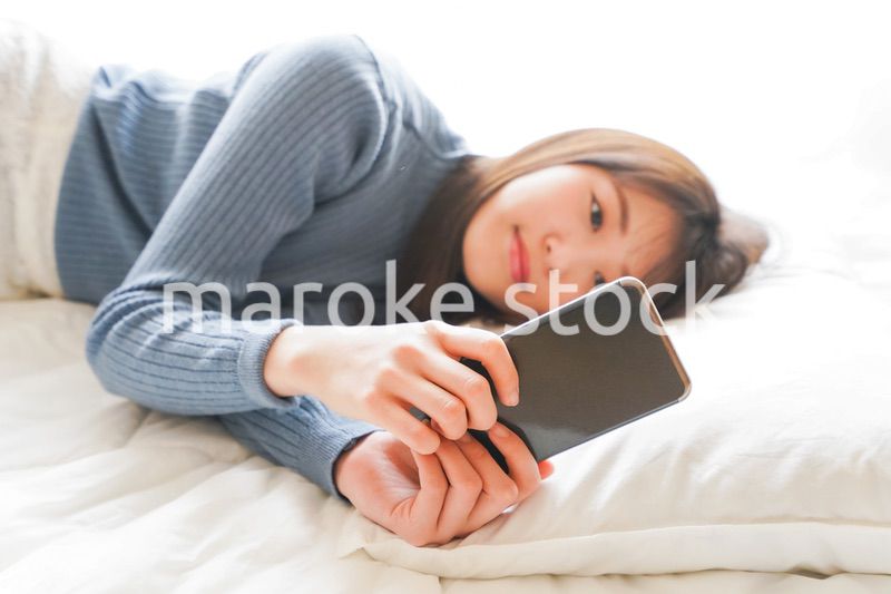 ベッドで寝る前にスマホを使う若い女性